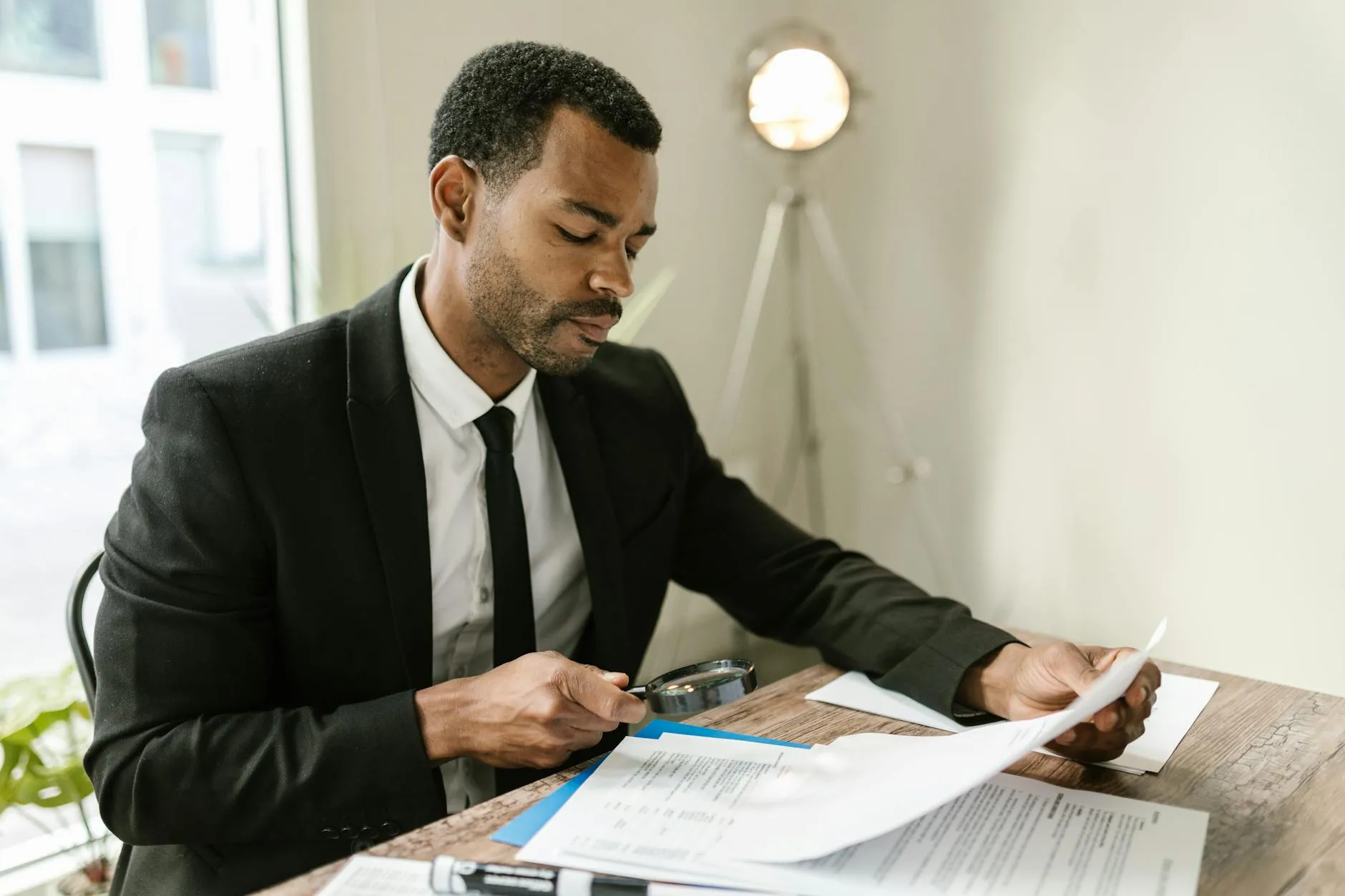 Professional examining paperwork with magnifying glass at office desk