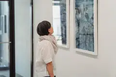 Woman in gallery intently examining abstract paintings up close