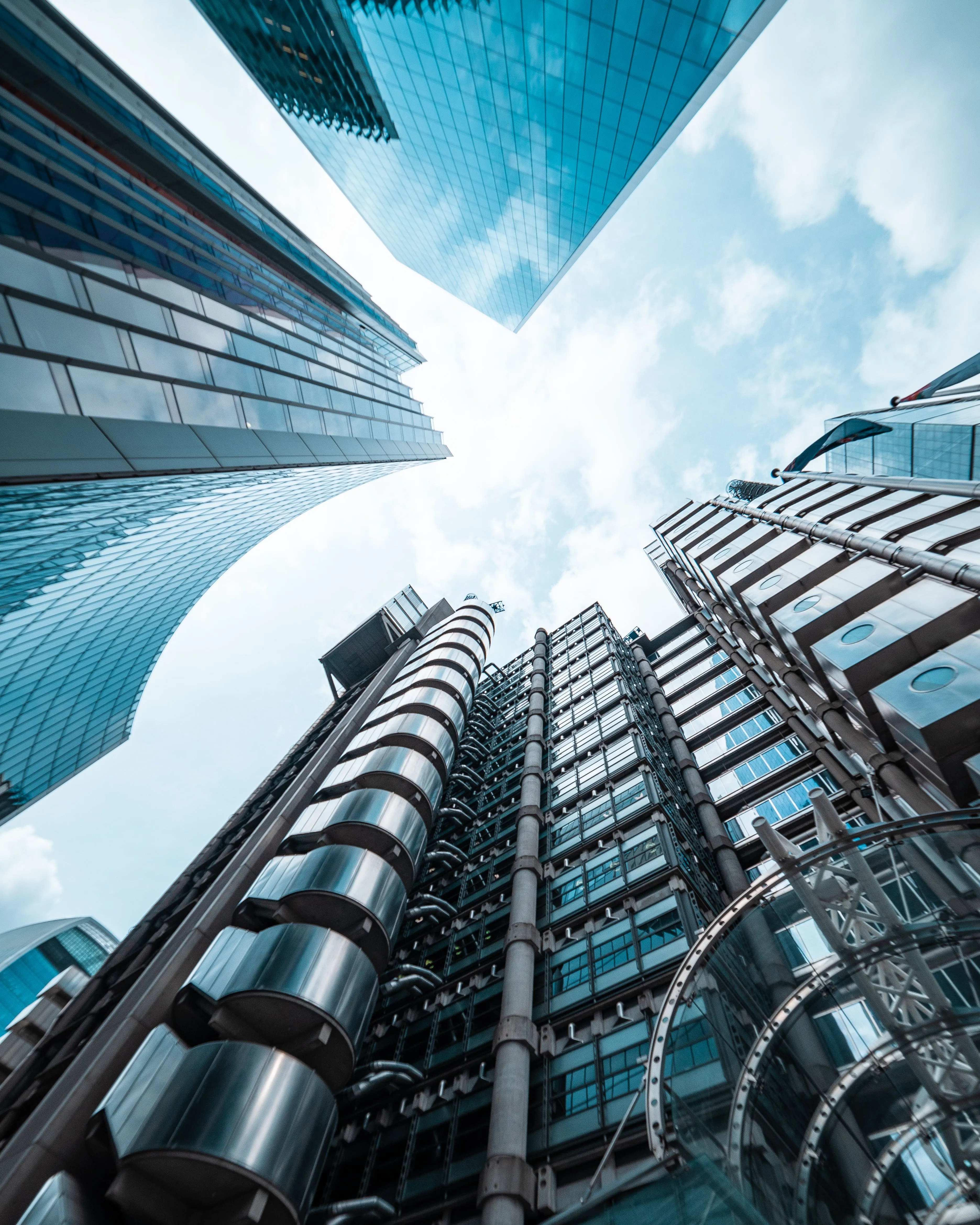 The Lloyd's building and the glass towers of Lime Street, City of London, seen from below against a bright sky