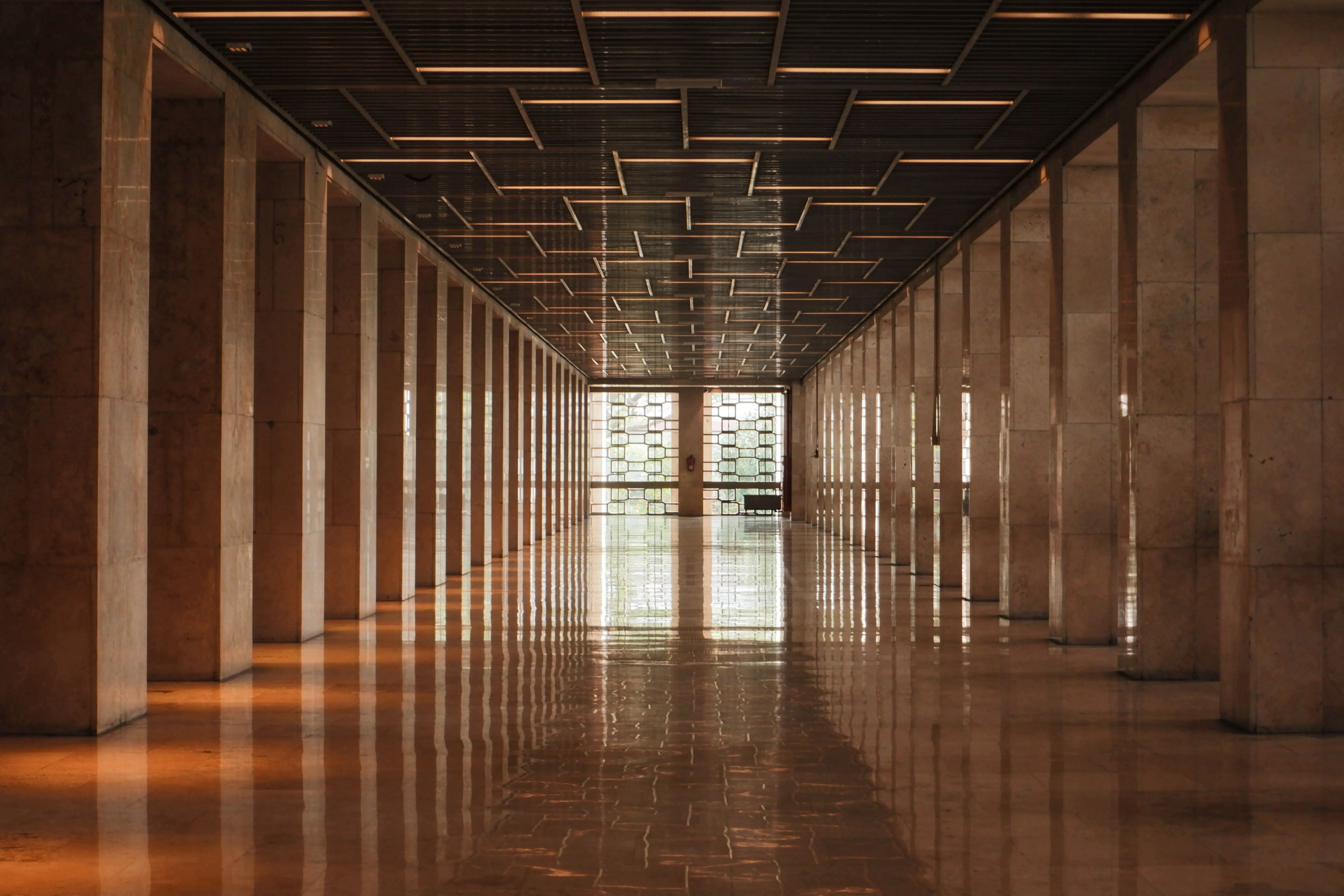 A marble corridor lined with columns under warm light, its floor reflecting the far window