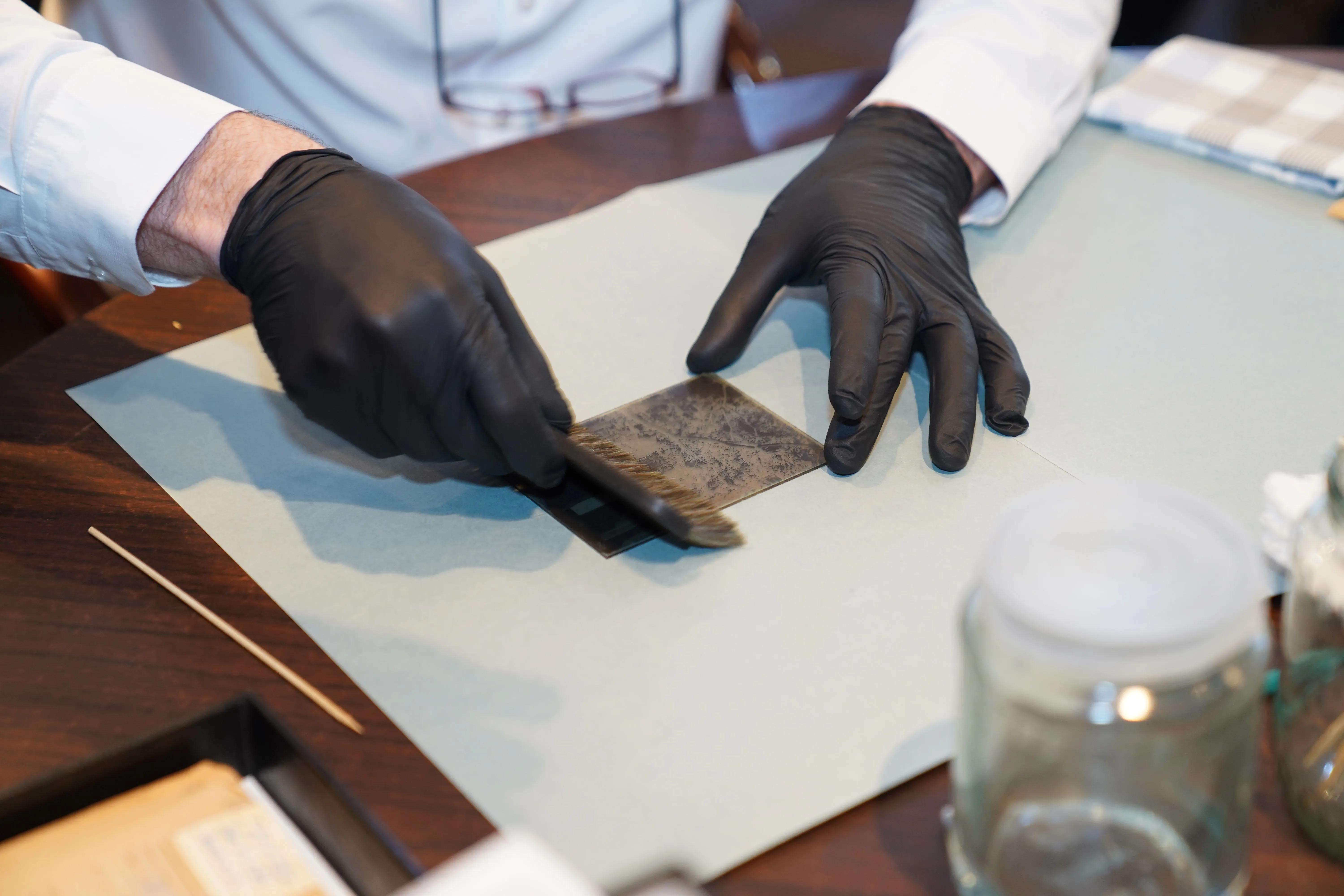Black-gloved hands brushing a daguerreotype on a worktable