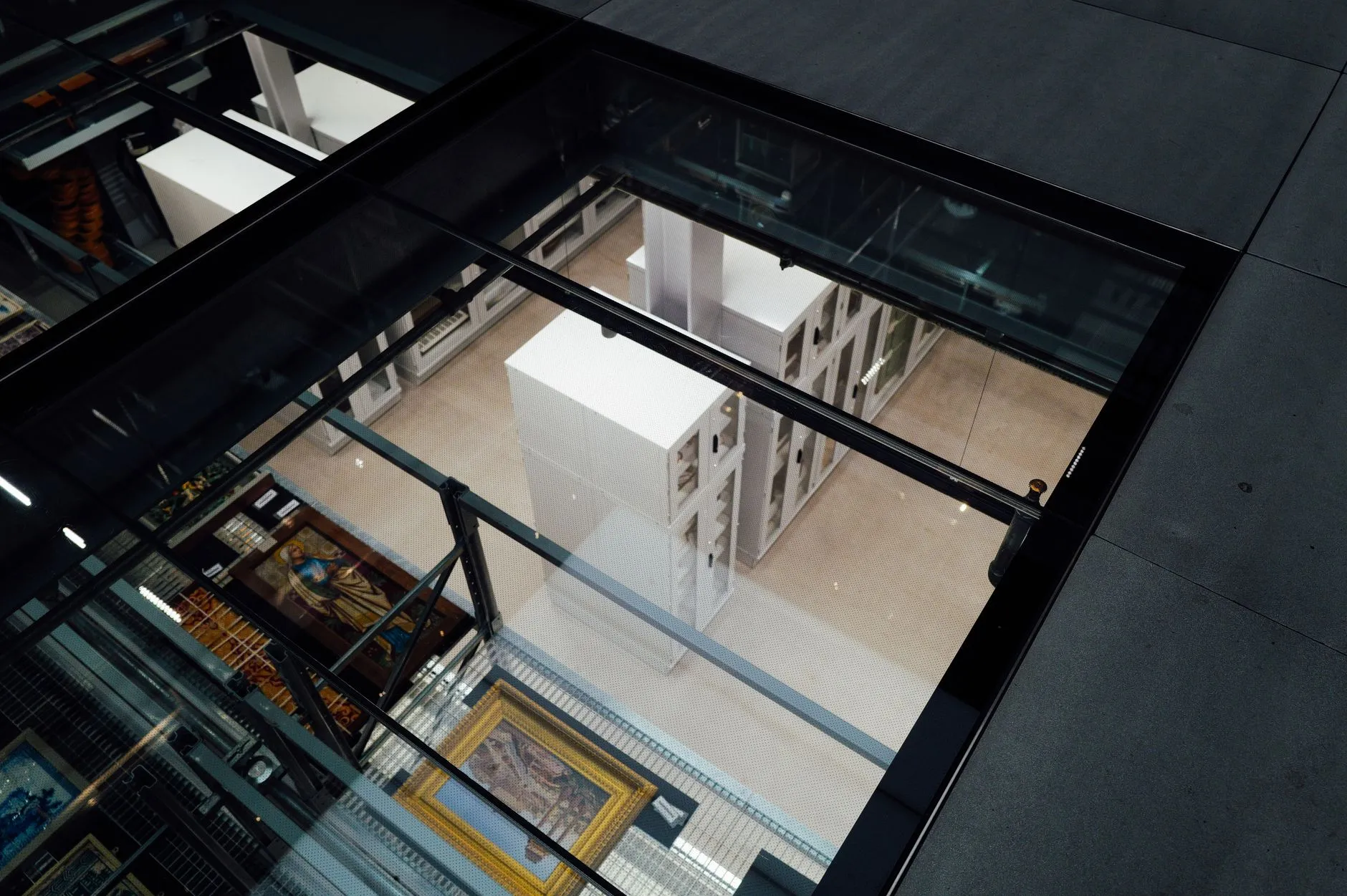 Art storage seen from above through a glass ceiling: racks of framed paintings and white crates. Photo by Adrien Olichon / Pexels.
