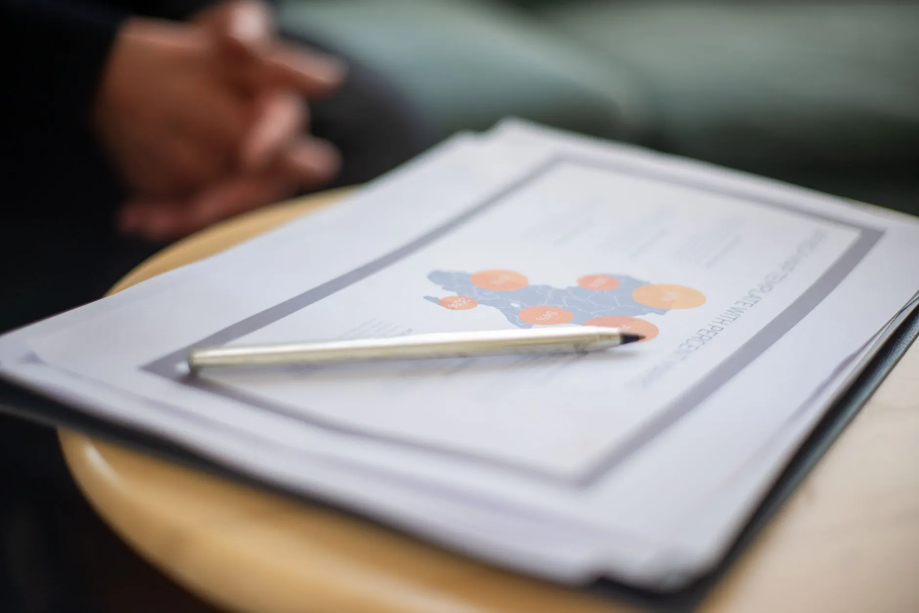 A bound report and a silver pen on a round table, in shallow focus. Photo by Kampus Production / Pexels.