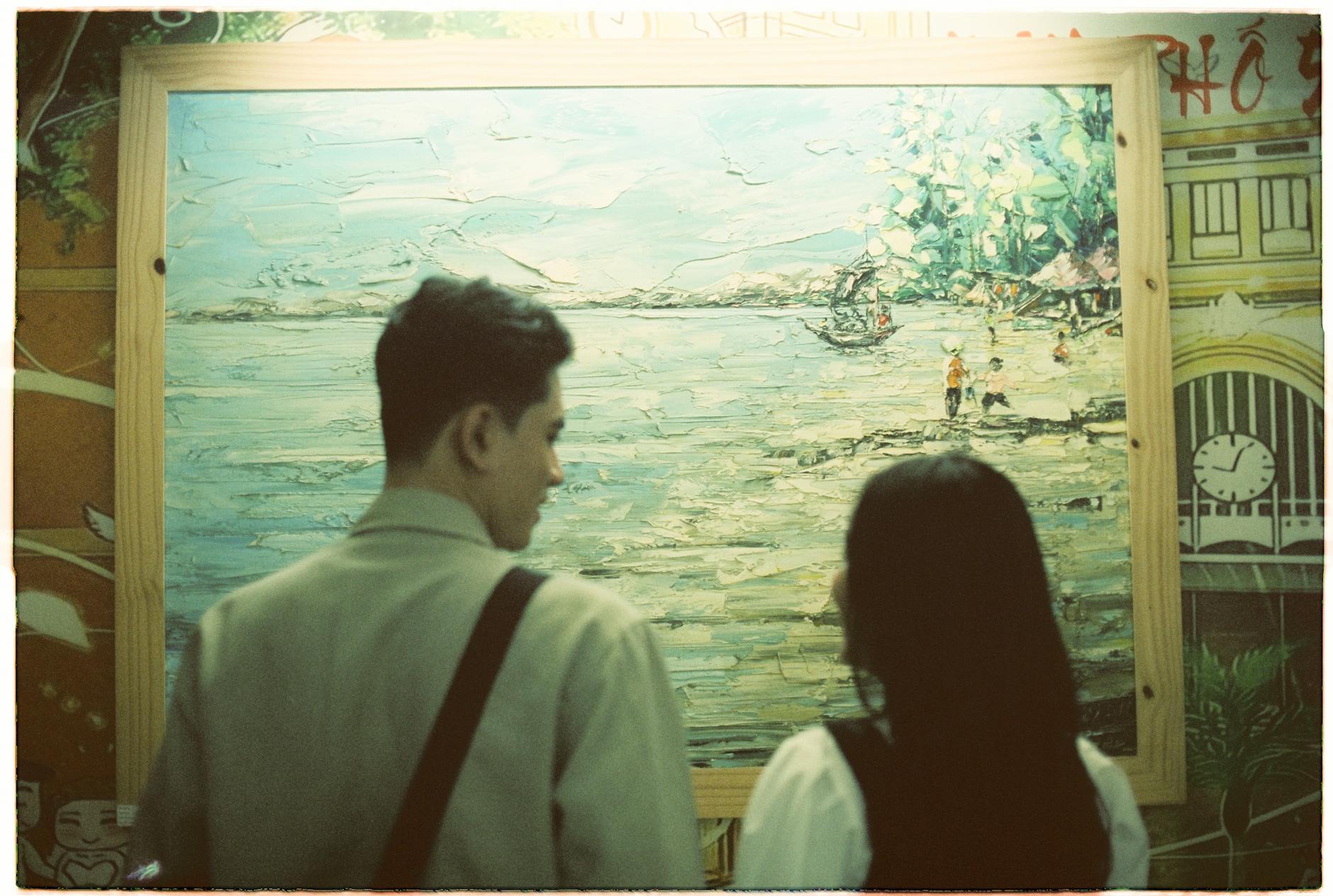Two visitors closely examining a painting in a gallery setting